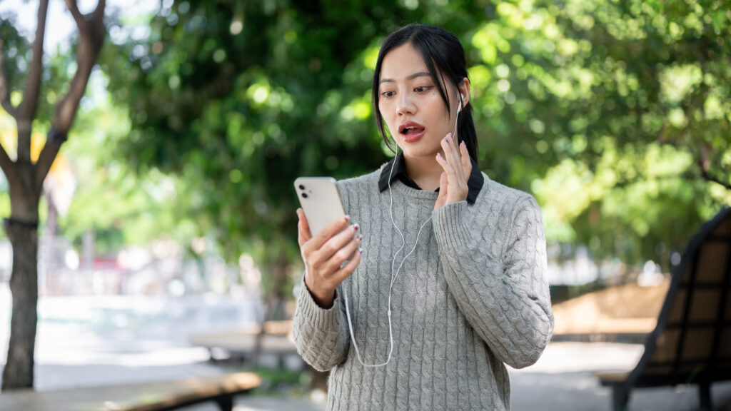 A charming Asian woman enjoys listening to music while walking along the footpath in a park. - Christian Counselors of Mooresville Limiting screen time can help you to relax and be in tune with your environment.